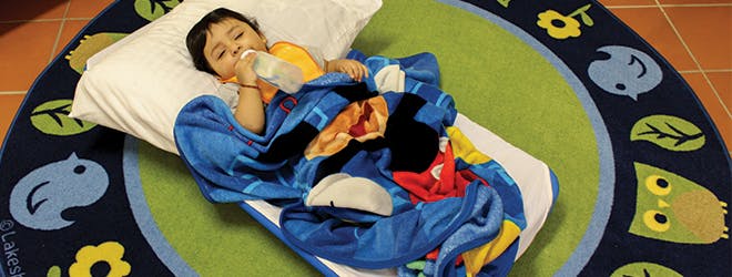 Child lying on a mat and drinking from a bottle