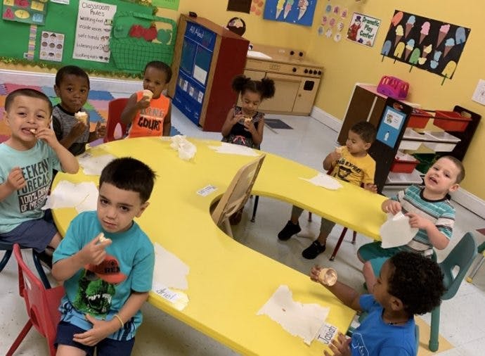 Children eating snacks at a yellow table in a classroom