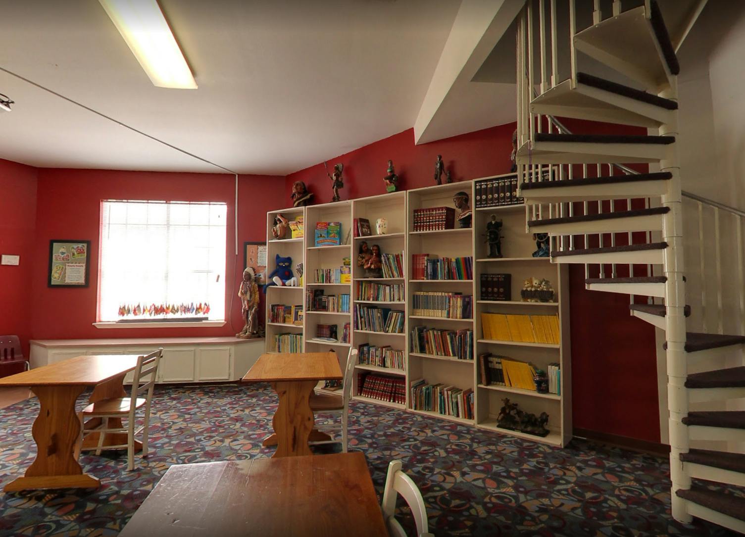Room with red walls, bookshelves, tables, and a spiral staircase