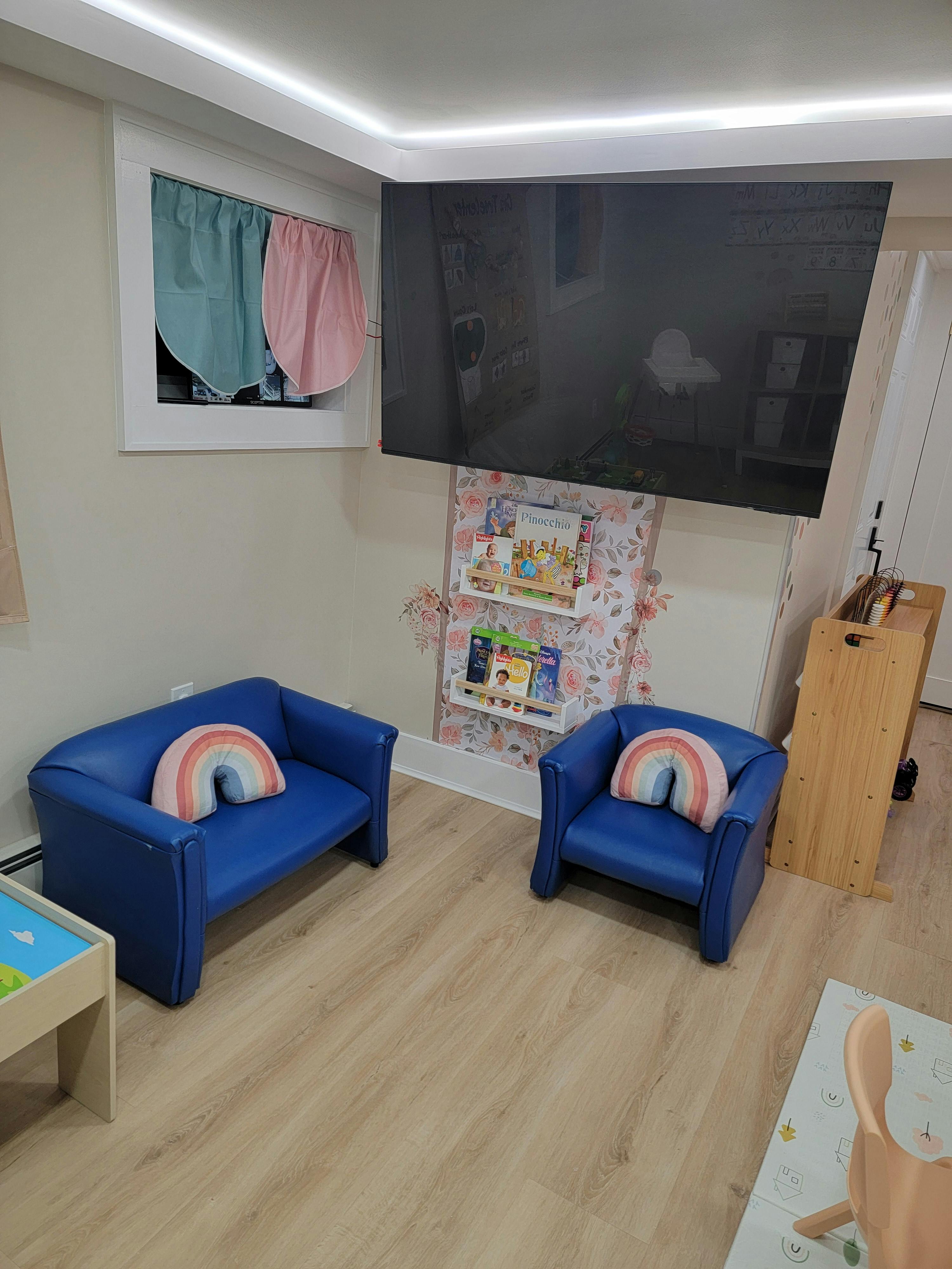 Two blue child-sized chairs with rainbow pillows in a room with a TV