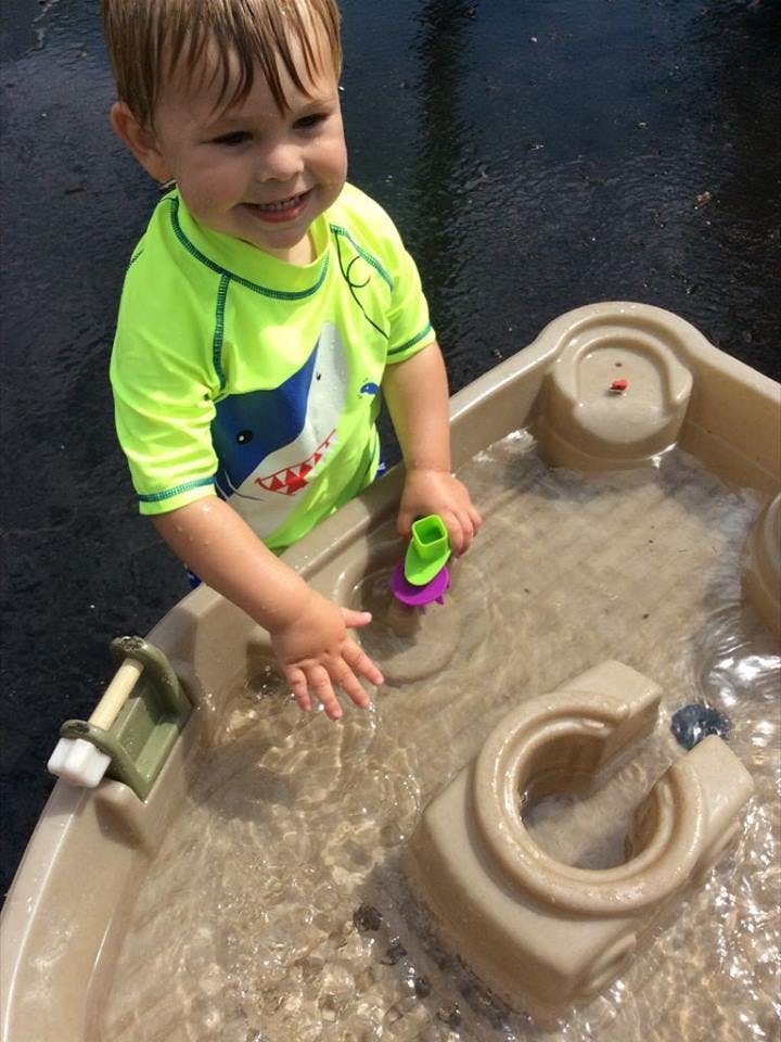 Child playing in a water table with a toy boat