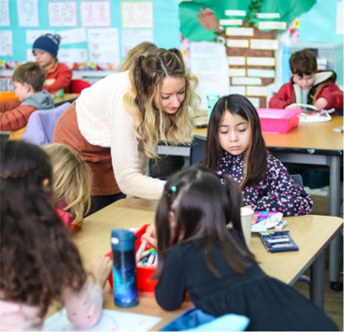 Adult helping children at desks in a classroom
