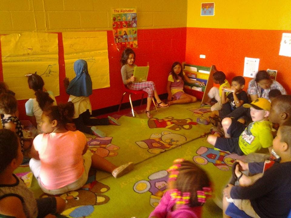 Children sitting on a rug in a classroom, one child reading aloud