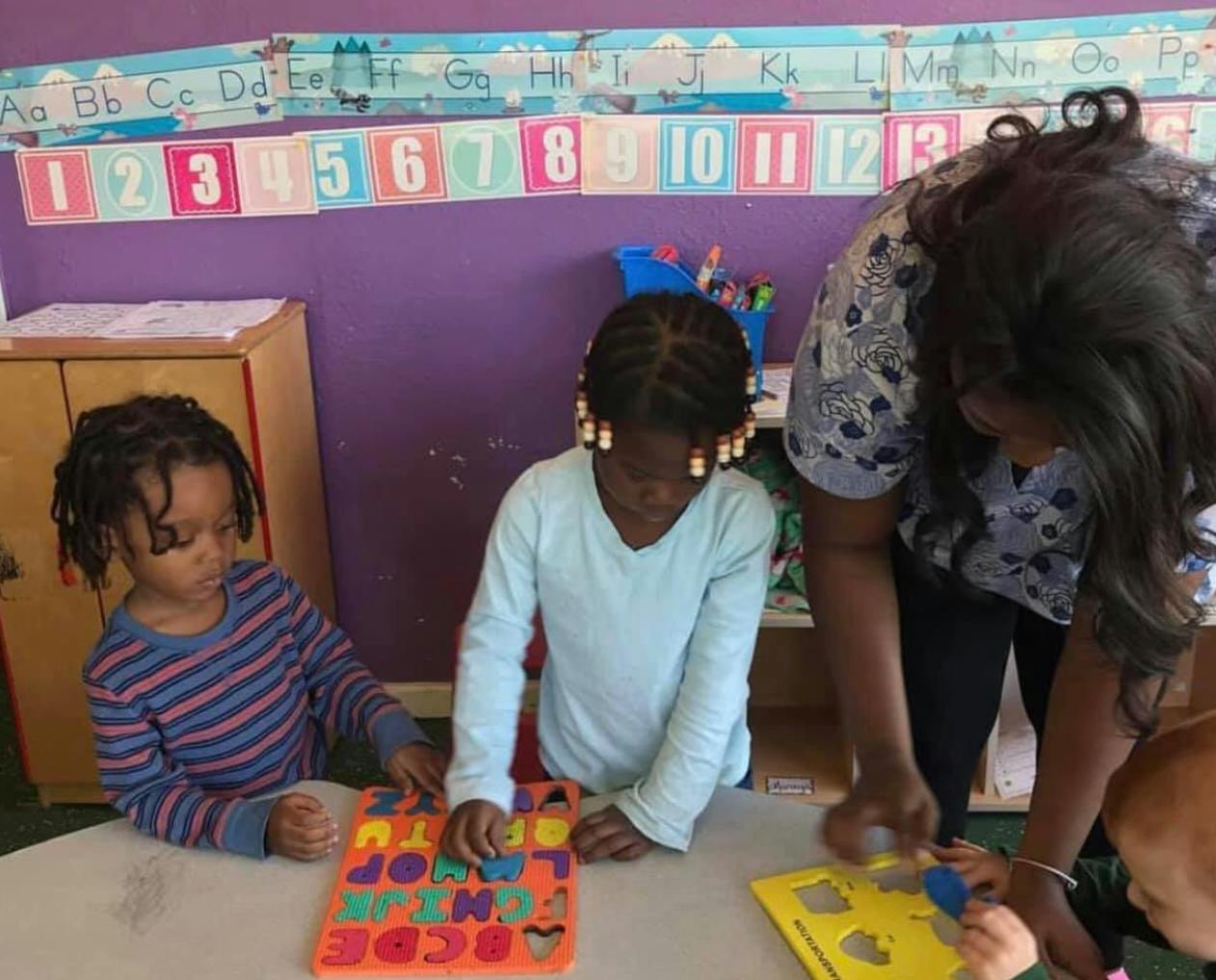 Two children and an adult playing with puzzles at a table in a classroom