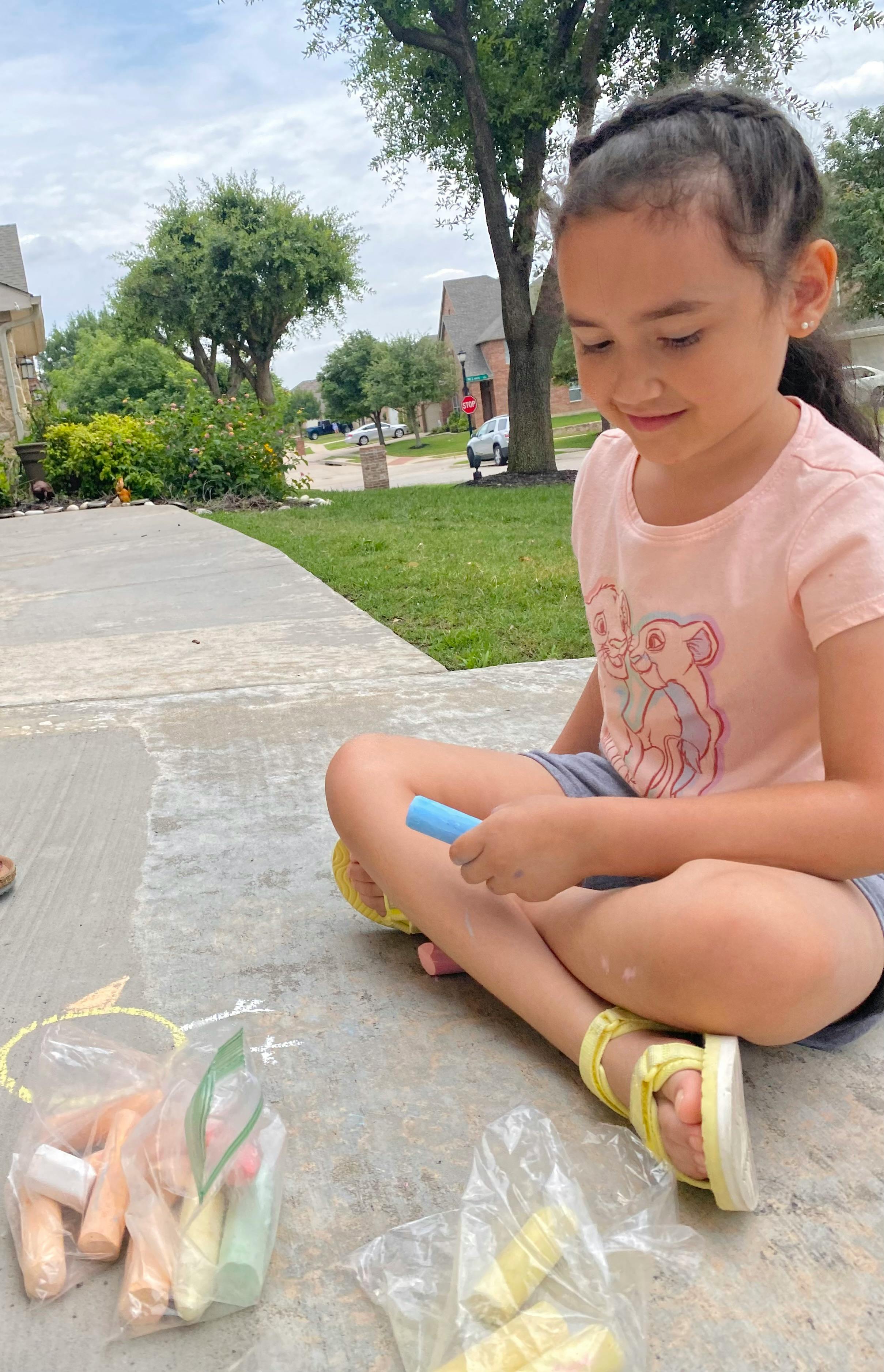 Child sitting on sidewalk holding chalk