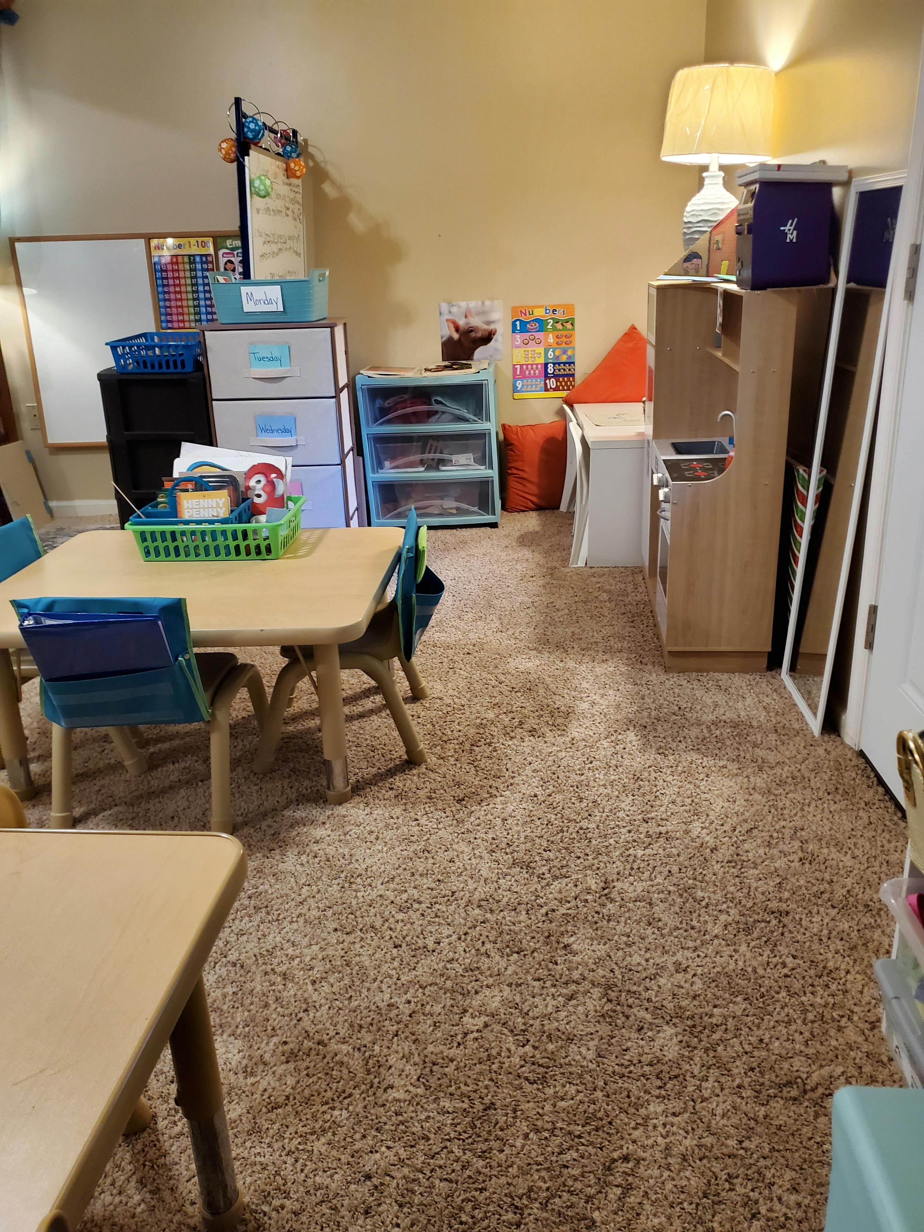 Classroom with small tables and chairs, storage units, and a play kitchen