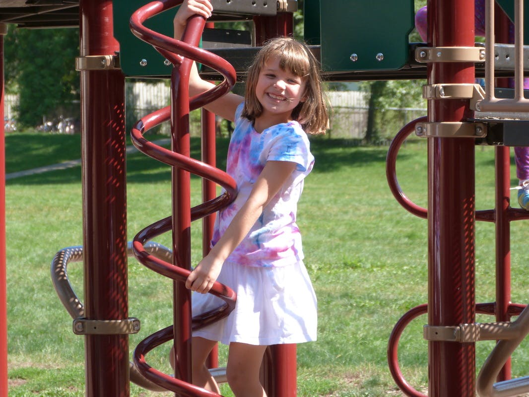 Child on a playground structure holding a spiral pole