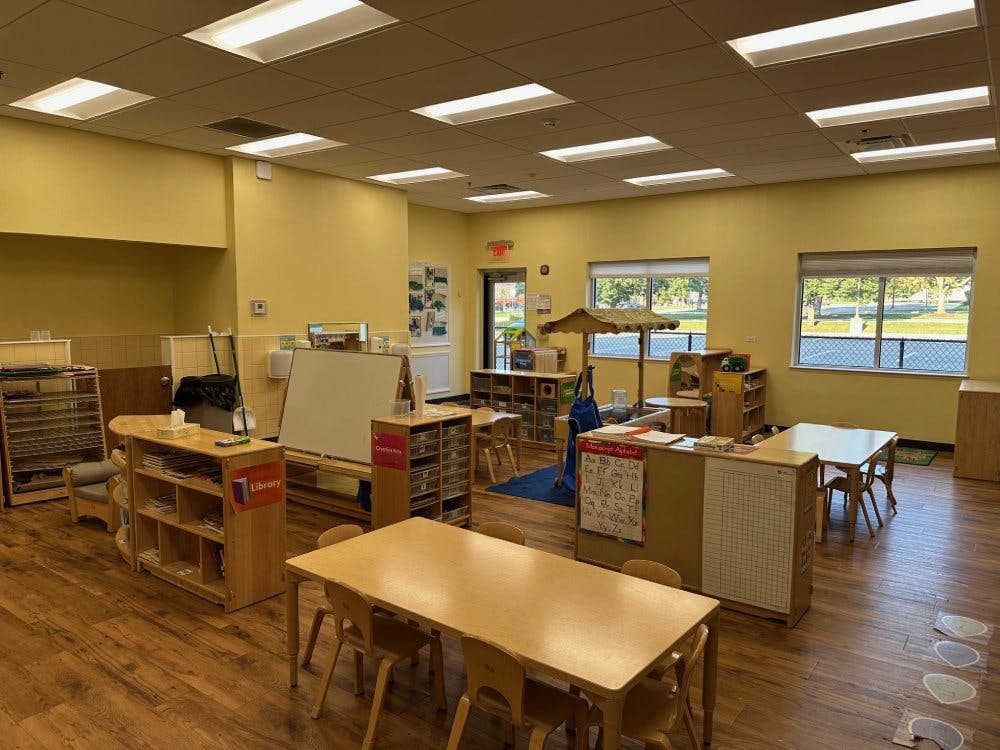 Empty classroom with small tables and chairs, shelves, and windows