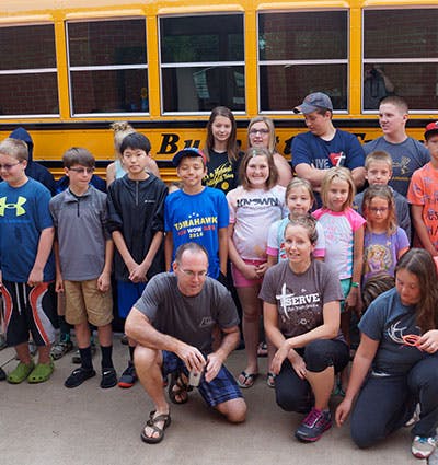 Group of adults and children posing in front of a school bus