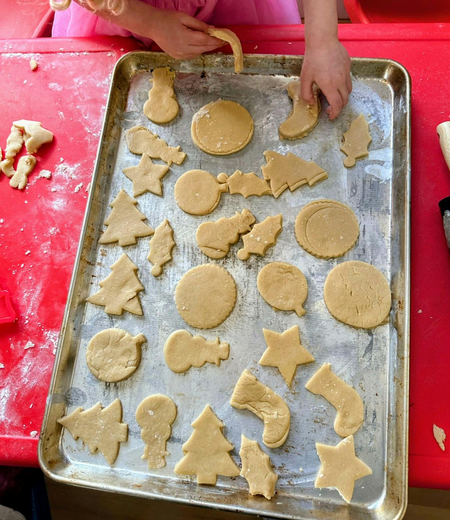 Child's hands arranging holiday-shaped cookie dough on a baking sheet