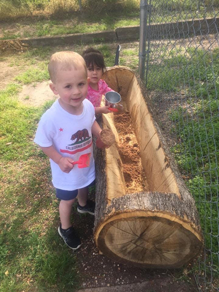 Two children playing with dirt in a hollowed-out log