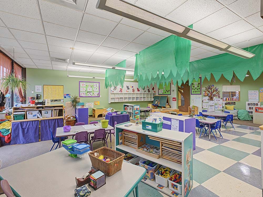 Classroom with tables, chairs, shelves of toys and books, and green decorations