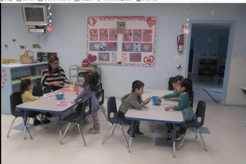 Adult and children seated at small tables in a classroom