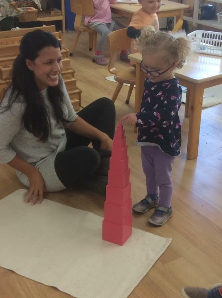 Adult and child playing with a pink tower in a classroom
