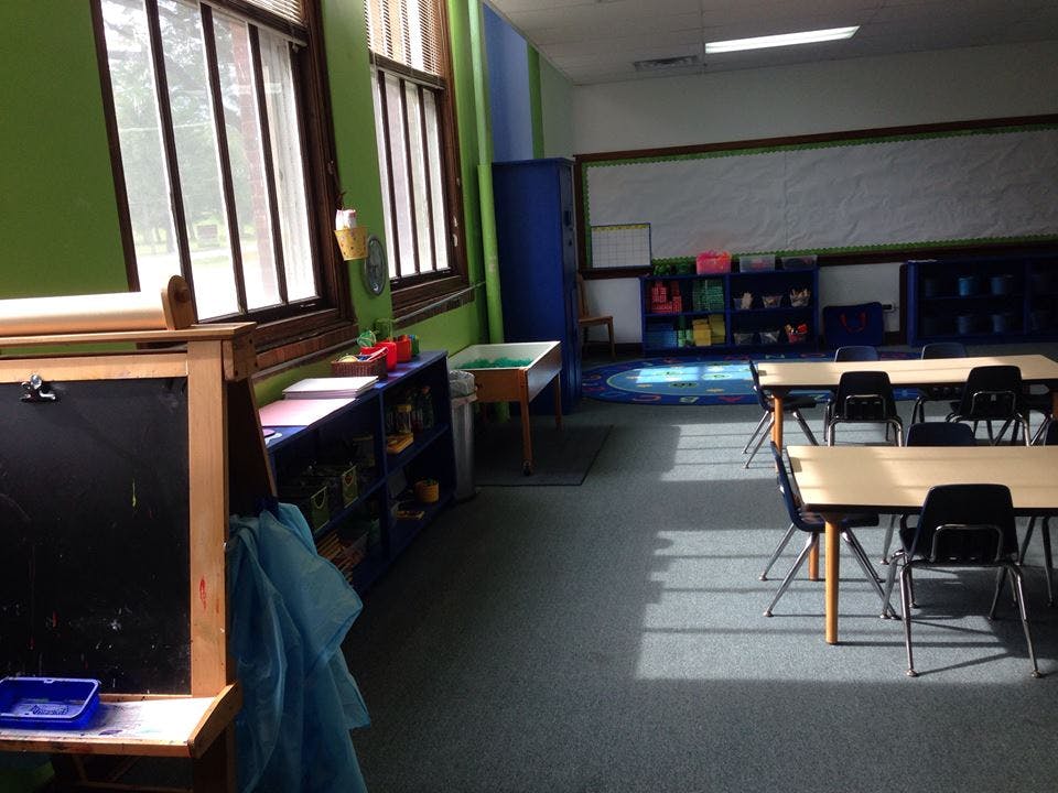 Empty classroom with tables and chairs, windows, and a chalkboard
