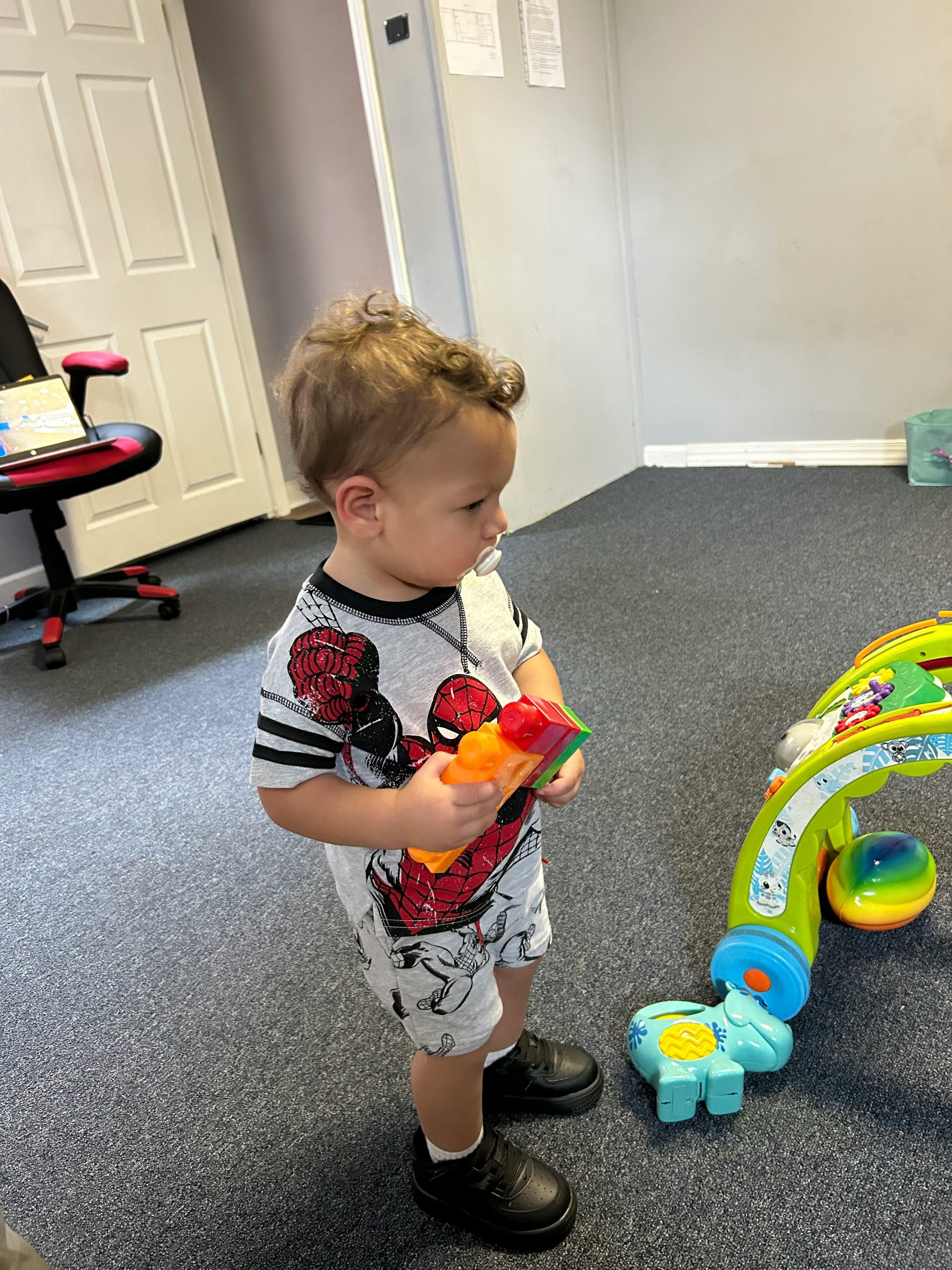 Child holding a toy while standing next to another toy
