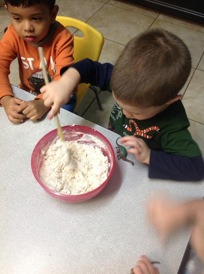 Child stirring a bowl of dough with a wooden spoon