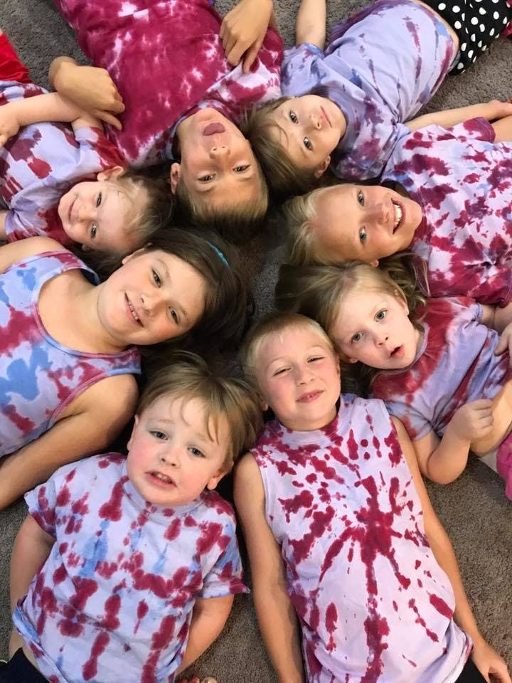 Group of children wearing tie-dye shirts, lying in a circle with heads together