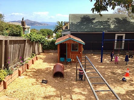 Children playing on a playground with a playhouse and climbing structure
