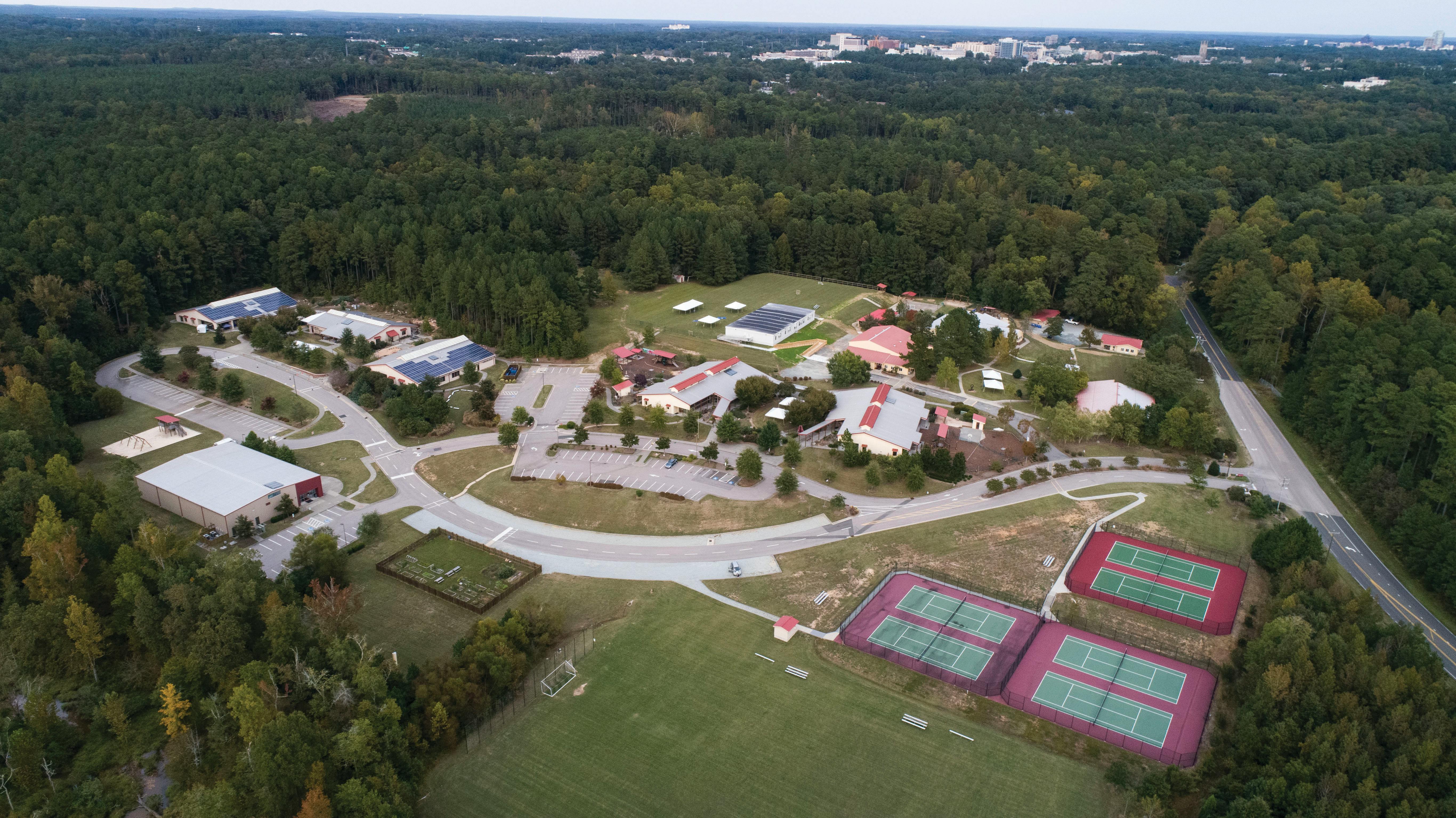 Aerial view of a campus with buildings, roads, and tennis courts surrounded by trees