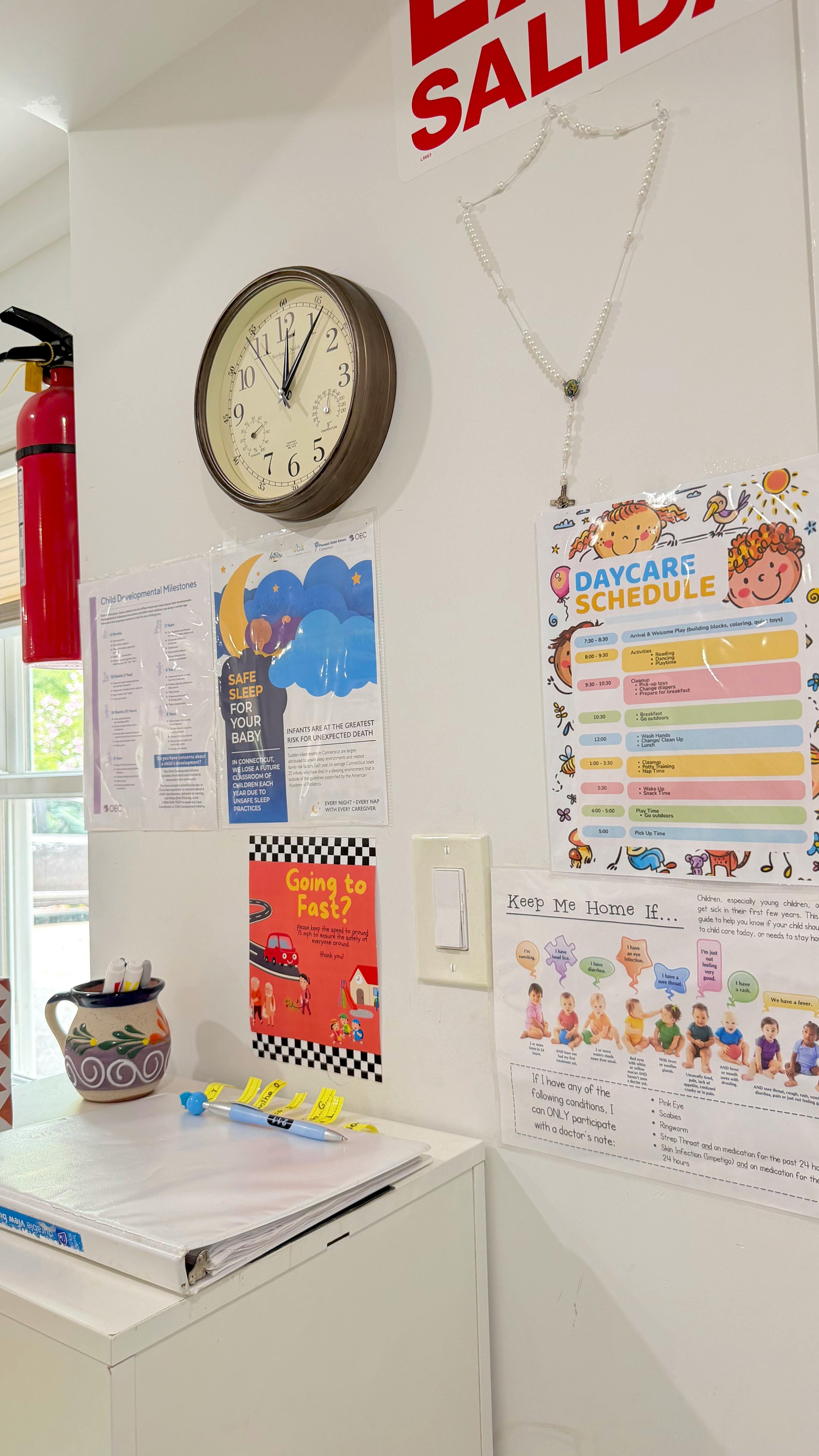 Wall with a clock and various informational posters and a daycare schedule