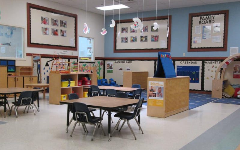 Classroom with small tables and chairs, shelves with toys, and wall displays