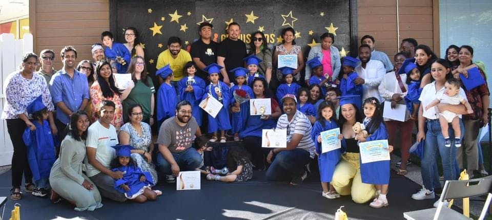 Group of adults and children in graduation caps and gowns holding certificates