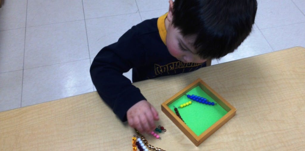 Child playing with beads and a small green tray on a table