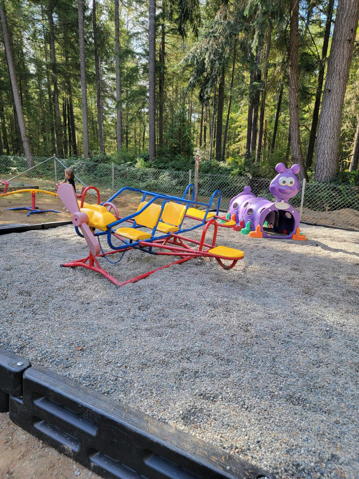 Playground with a red and yellow seesaw and a purple caterpillar tunnel