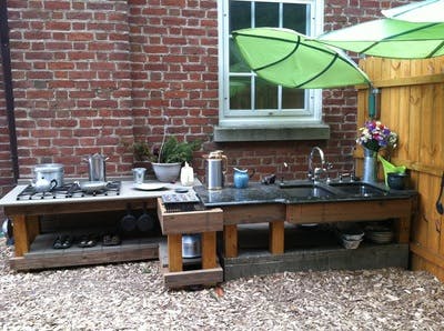 Outdoor kitchen with a stove, sink, and green umbrellas