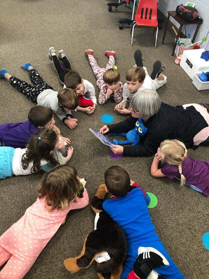 Adult reading a book to children lying on the floor in a circle