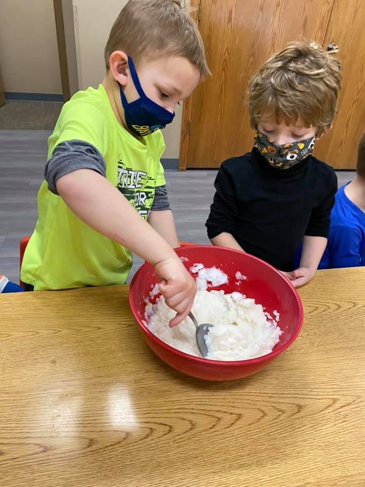 Two children in masks mixing a white substance in a red bowl