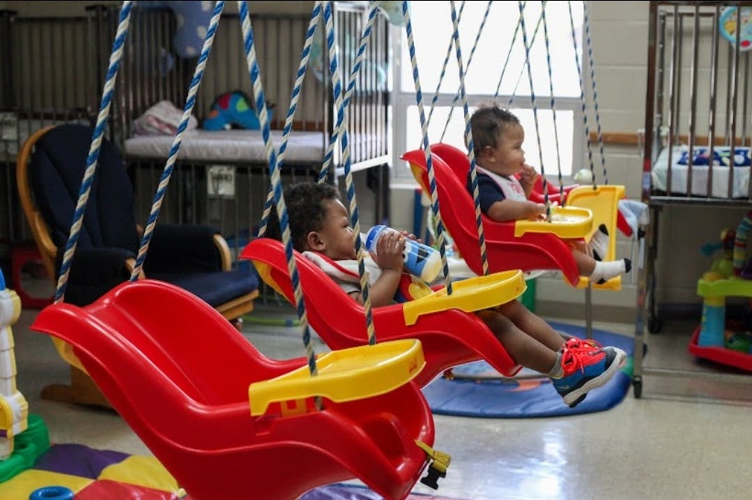 Two children sitting in red and yellow swings indoors