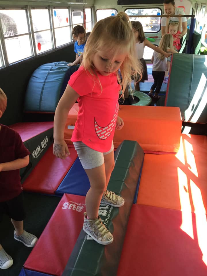 Child balancing on a beam inside a bus with other children