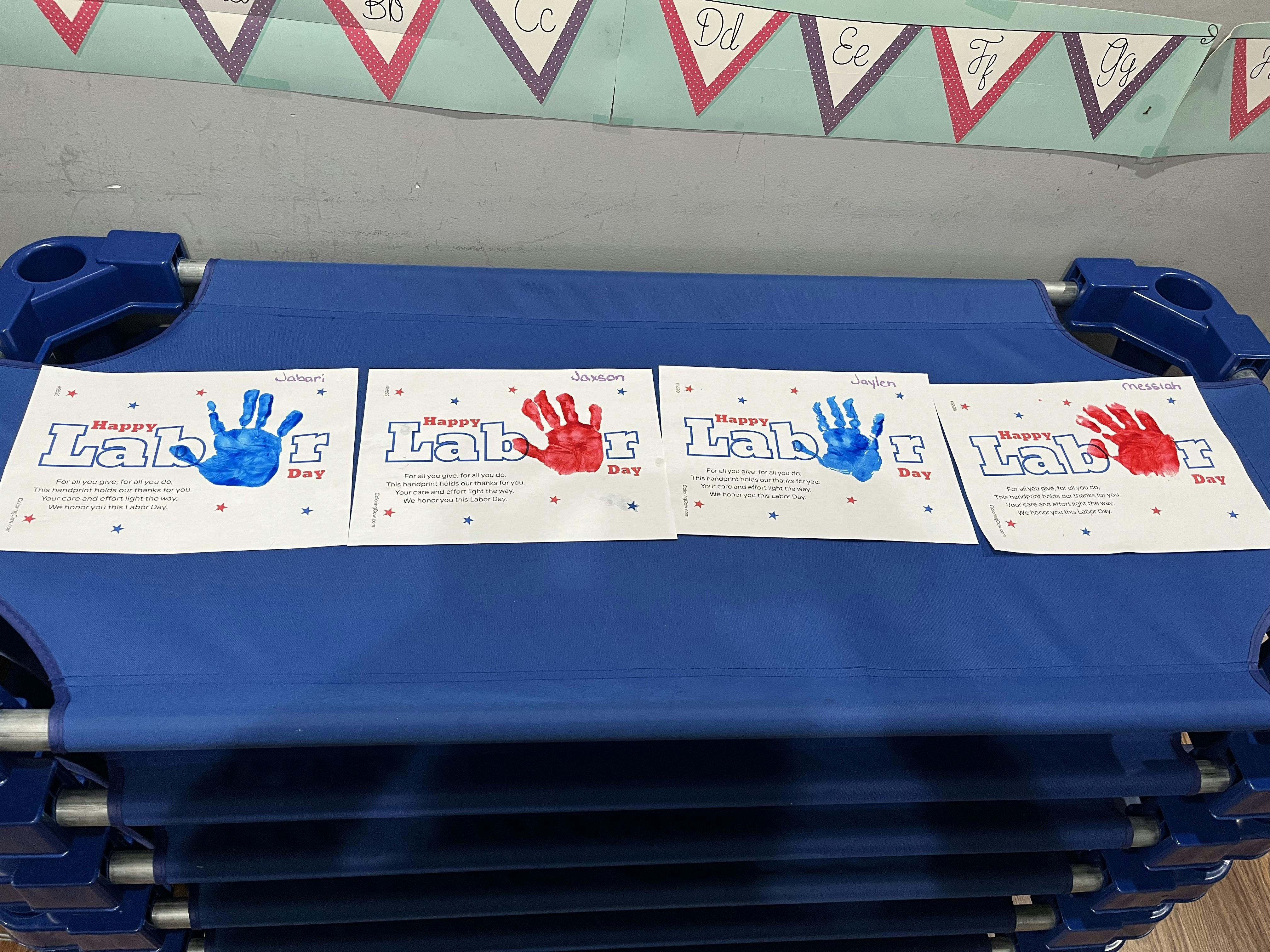 Four papers with handprints and "Happy Labor Day" text on blue cots