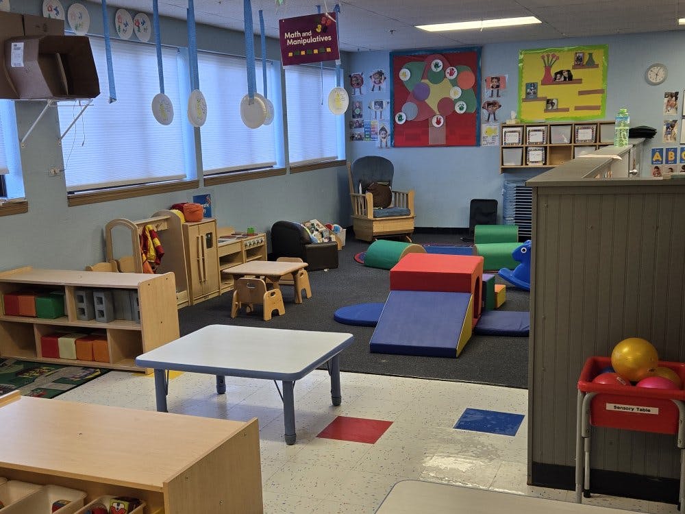 Children's classroom with small tables, play area with soft blocks, and various educational posters