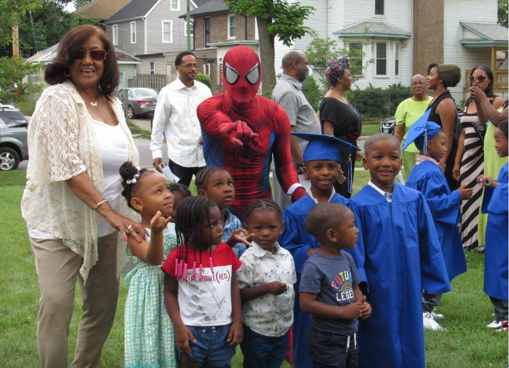 Person in Spider-Man costume with adults and children, some in graduation gowns