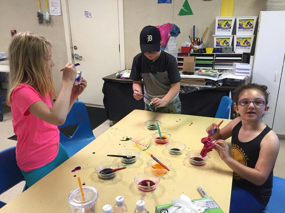 Three children painting at a table in a classroom