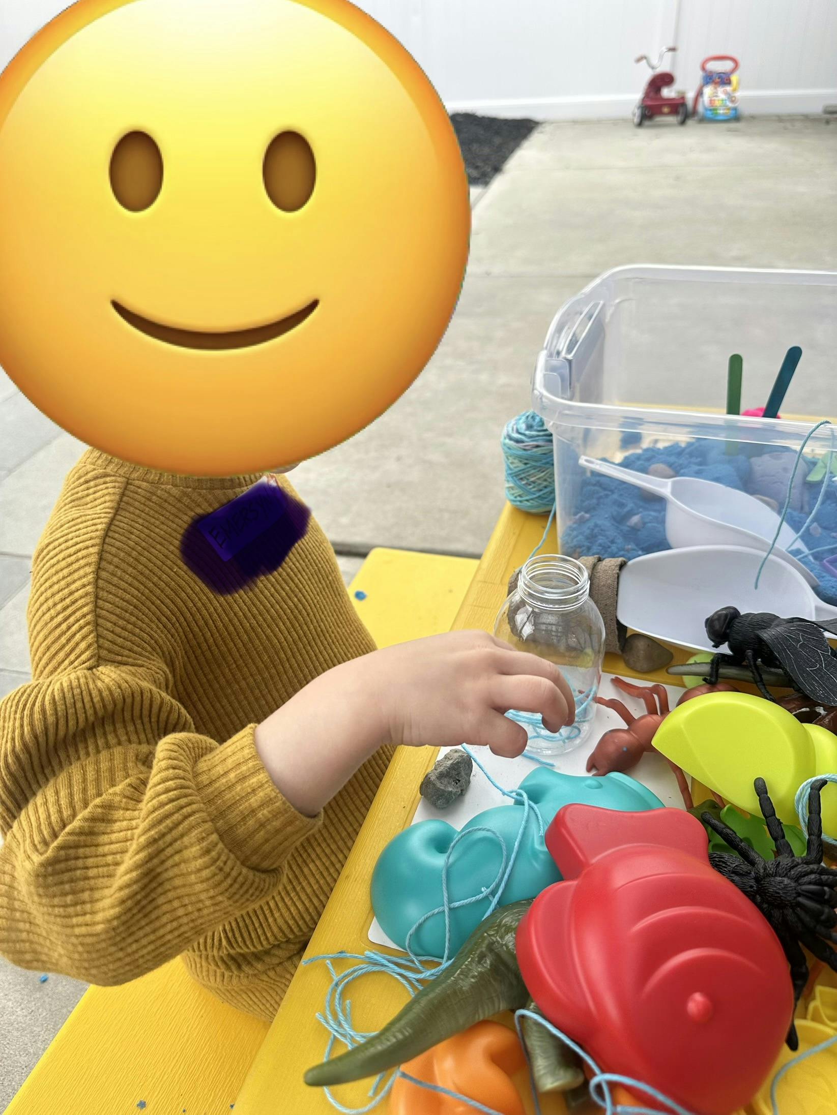Child playing with a sensory bin containing blue kinetic sand and toys