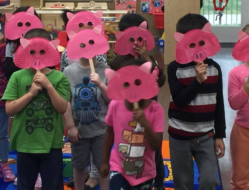 Children holding pink pig masks over their faces