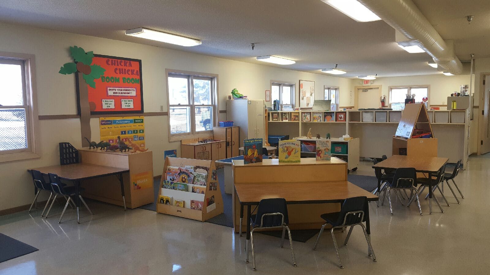 Classroom with small tables and chairs, shelves with books, and a "CHICKA CHICKA BOOM BOOM" sign