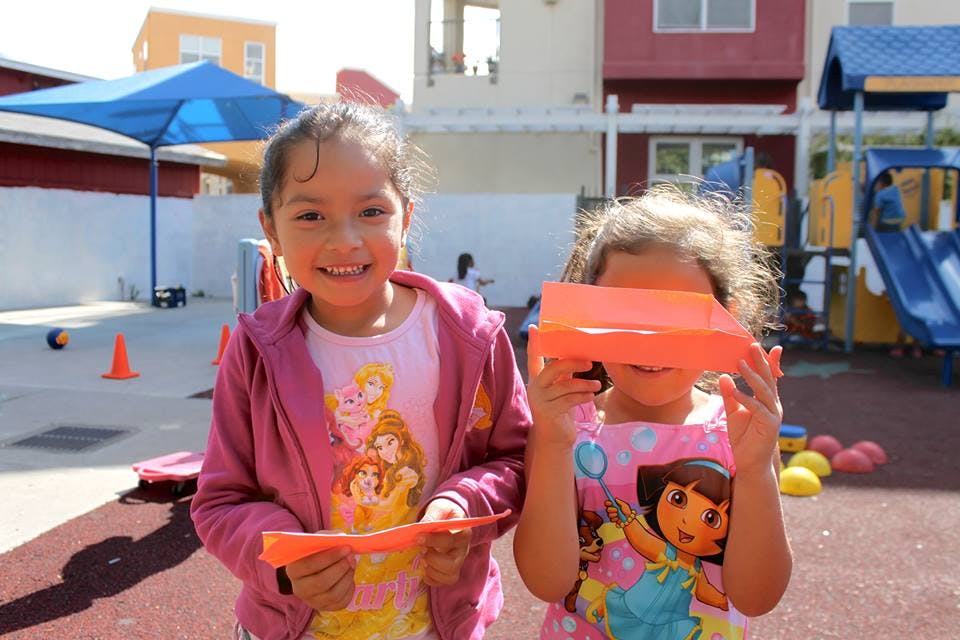 Two children holding orange paper, one smiling at the camera
