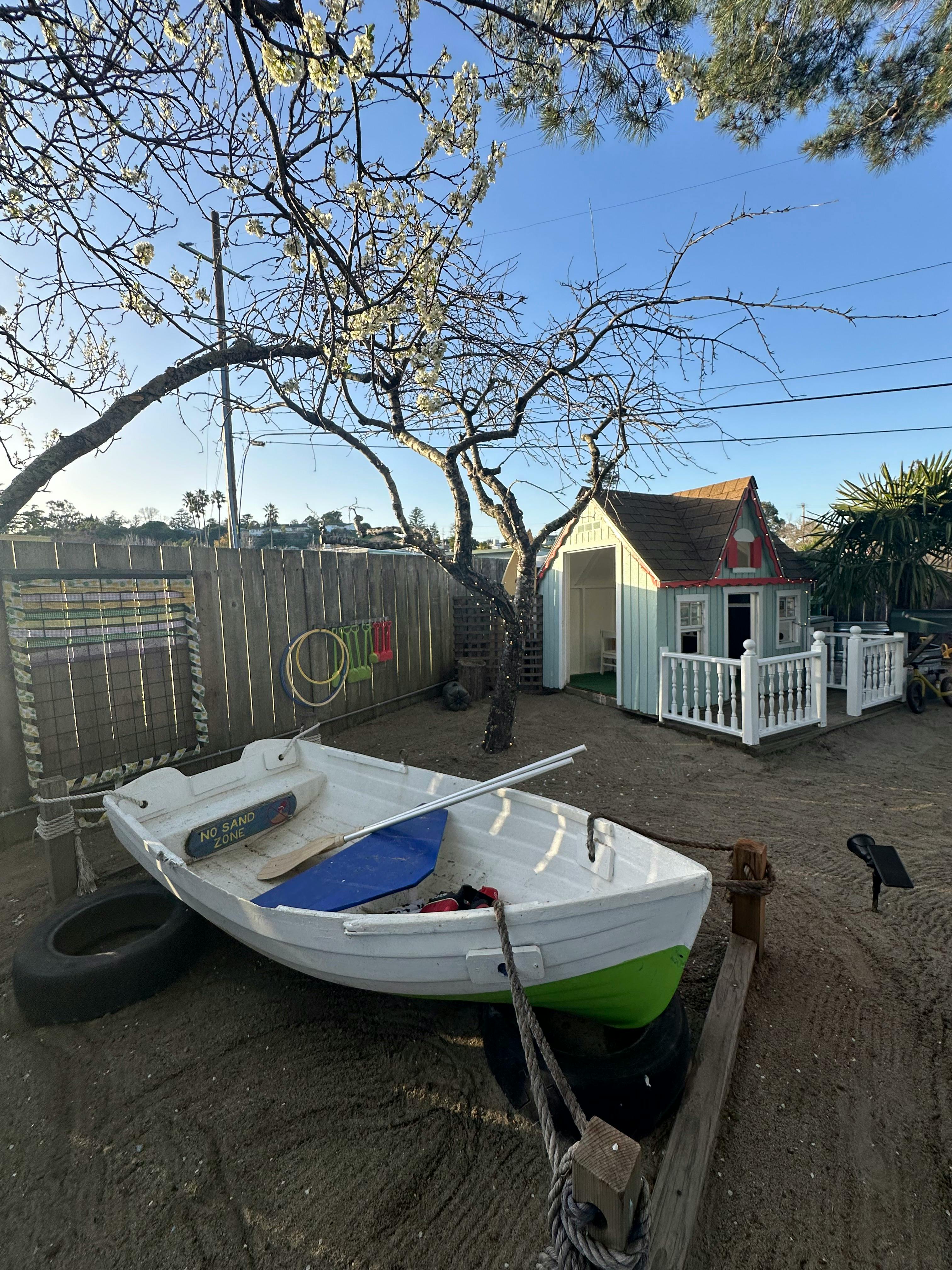 Small boat on dry ground next to a fence and a miniature house