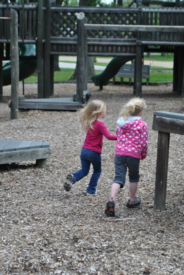 Two children walking on wood chips in a playground