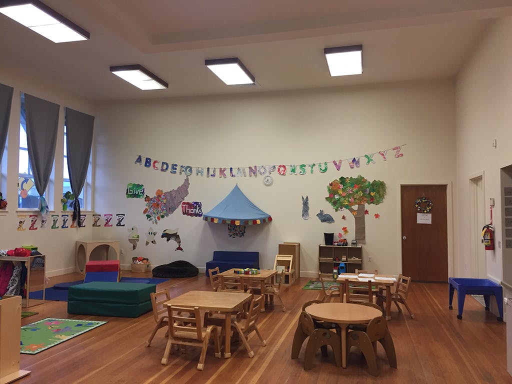Empty classroom with small tables and chairs, alphabet banner, and wall decorations