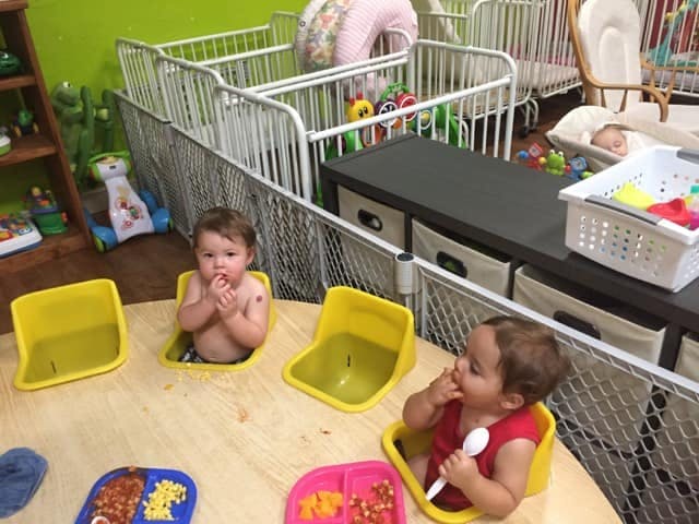 Two children in yellow chairs at a table, one eating