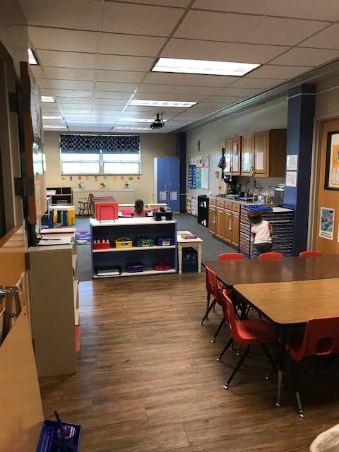 Classroom with tables, chairs, and a child near shelves
