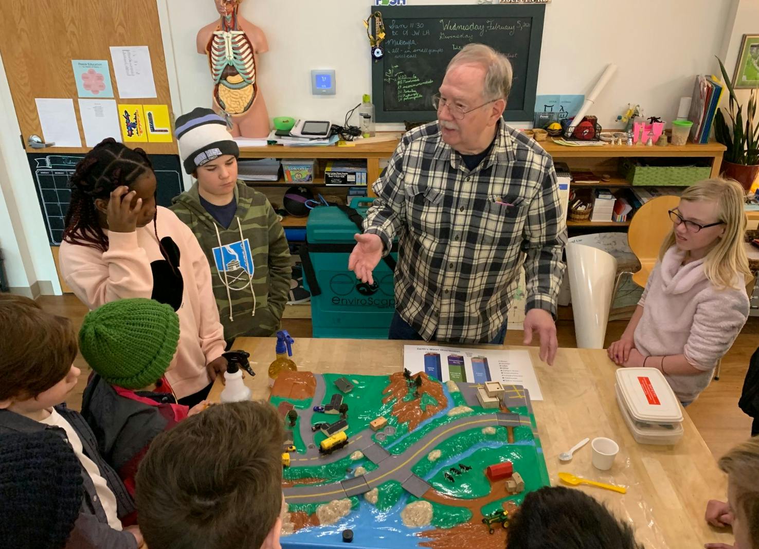 Adult person speaking to children gathered around a model landscape