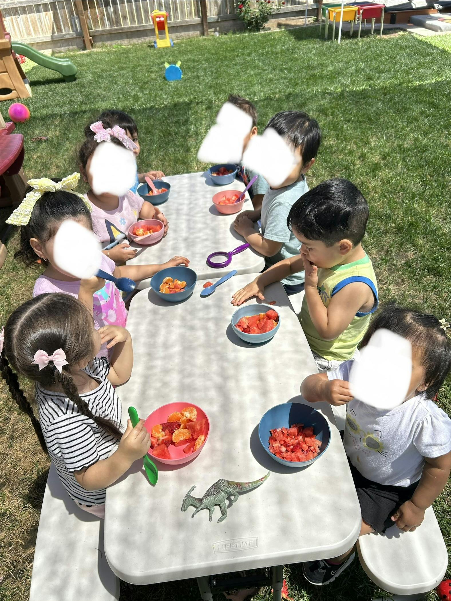 Children eating fruit at a table outdoors