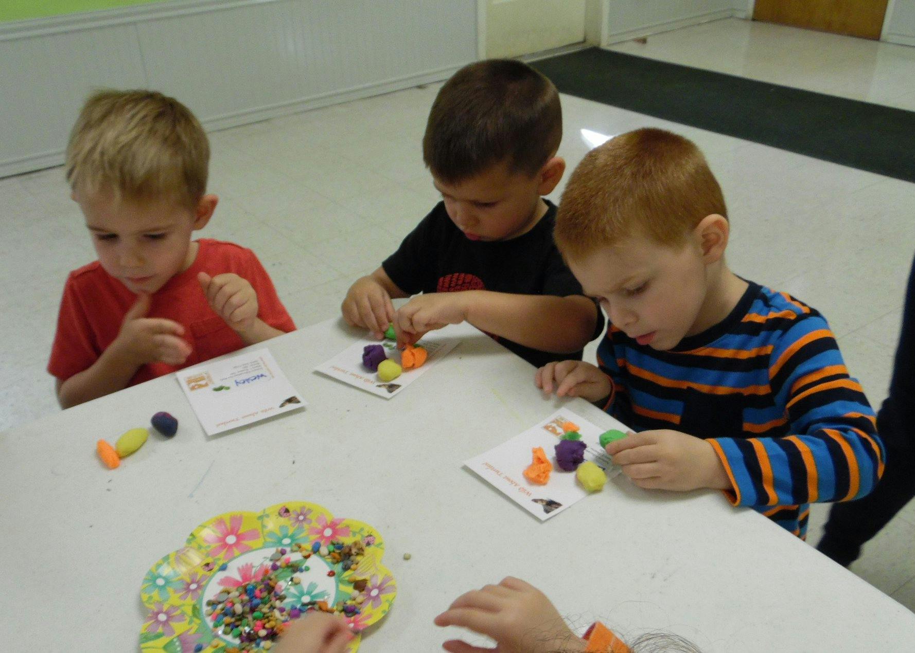 Three children at a table playing with colorful craft items